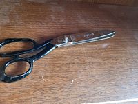 Photo of a large tailor's scissors with black handles and rusted silver steel blades stamped 'SHEFFIELD' on a wooden surface.