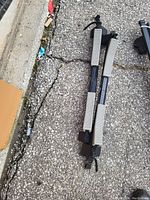 Photograph of two black metal roof racks with mounting clamps placed on an asphalt surface.