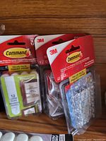 Three original retail packs of 3M Command damage-free hanging wall hooks on a wooden surface, showing packaging and labels clearly.