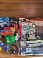 Photo of assorted office and art supplies including tapes, markers, pens, scissors, staples, and glue.