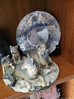 Photo shows a shelf displaying a wolf figurine with multiple wolves and a blue-silver decorative plate depicting wolves.
