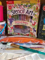 Photo of Klutz Stencil Art kit box, paintbrushes, paint palette, and paints on tabletop.