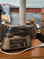 Photo of the Dayex electric stripper machine with a transparent plastic protective cover and attached power cord.