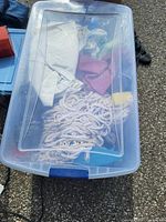 Top view of plastic tote with mop rope, cleaning cloths and sponges visible inside.