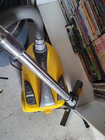 Yellow Europro Rally 2 canister vacuum cleaner with metal wand and floor cleaning head positioned on floor near shelves.