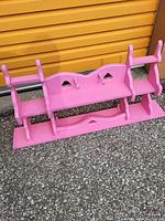 Pink wooden wall shelf with two levels, heart-shaped cutouts, and a small drawer on the bottom tier, photographed outdoors against a yellow garage door.