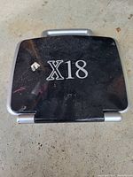 Closed black and silver hard case with handle, labeled 'X18' on top, showing surface wear.