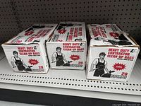 Three unopened boxes of heavy duty contractor clean-up bags on a store shelf.