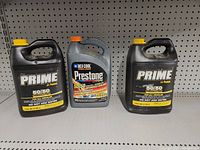 Three 1-gallon jugs of antifreeze/coolant on shelf. Two Prime brand on sides and one Prestone DEX-COOL brand in middle.