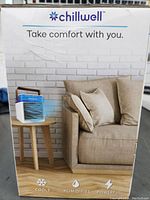 Front view of Chillwell portable air conditioner unit on small wooden table next to beige couch, showing product branding and design.