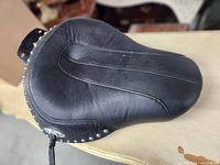 Top view of black leather motorcycle seat showing contoured stitching and studded edge