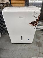 Front view of Insignia dehumidifier showing brown paint splashes on white body.