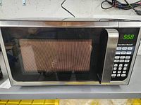 Stainless steel Hamilton Beach microwave with digital control panel, showing time on display 5:58, powers on.