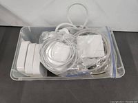 Plastic bin containing multiple Apple power adapters and cables, some bundled in plastic bags.