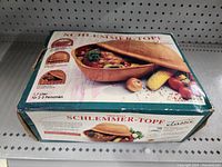 Box front showing the Schlemmer-Topf Classic clay baker with food inside and vegetables around it, 1.7 liter size for 2-3 persons.