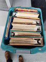 Top view of the plastic tote containing multiple scrapbooks in ring binders of various colors and thickness.