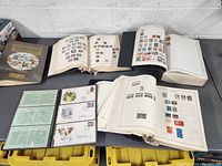 Five stamp collections displayed on a table including albums, loose pages with stamps, and first-day covers.