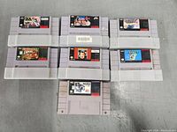 Top view of all seven Super Nintendo game cartridges laid out on a flat surface, showing front labels and cartridge casing.