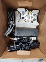 Photo of Xbox 360 console, two white wireless controllers, power supply, AV cable, and Kinect sensor packed inside a box.