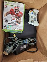 Photo of Xbox 360 console, white controller, NCAA Football 09 game, power supply and AV cable in a box.