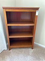 Front view of wooden bookcase showing three shelves and medium brown wood finish.