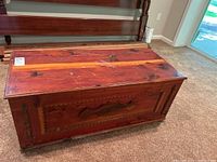 Top and part of the front side of the cedar chest showing stained wood surface and reddish finish, as well as carved wooden moldings.
