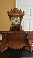 Photo of mantel clock showing carved wooden frame and glass clock face with Roman numerals