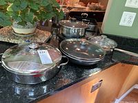 Photo showing set of cookware on countertop including casserole pan, frying pan, and stock pot with lids.