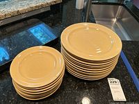 Stack of 12 large cream-colored dinner plates with a subtle raised circular pattern near center, placed on countertop.