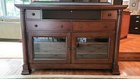 Front view of entertainment center showing open electronics shelf, two drawers and glass-front cabinet doors