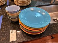 Stack of eight colorful Fiestaware plates alongside five nested bowls on a granite countertop near a kitchen sink.