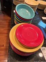 Stack of colorful ceramic plates and bowls in various colors including red, yellow, blue, orange, and turquoise.