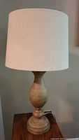 Full view of one table lamp showing beige wooden base and off-white fabric shade