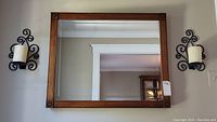 Wood framed beveled mirror with metal wall sconces featuring battery operated candles mounted on either side of the mirror.