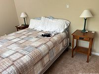 Photo showing two wooden nightstands placed beside a bed, each with a lamp on top, showcasing their size and condition in a bedroom setting.