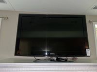 Front view of Samsung flat panel TV on a white mantel with a remote placed on the base of the TV.