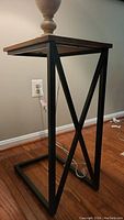 Side view of one wooden top side table with a black metal geometric frame base on hardwood floor.