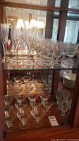 Glass cabinet shelves containing multiple sizes and styles of clear stemware glasses including Perrier-Jouet branded flutes and various other types.