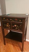 Front view showing the table's three drawers with detailed floral painting, lower shelf, and overall wooden structure.
