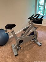 Full view of silver Tsunami indoor cycle on carpet, showing frame, seat, handlebars and base