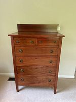 Front view of the vintage wooden chest of drawers showing five drawers, two small top drawers and three larger bottom drawers, with brass circular handles and keyholes on the top drawers.