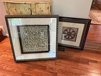 Overview photo of two framed brownstone resin wall art pieces resting on hardwood floor, showing sizes and frames.