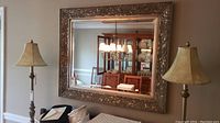 Full view of framed mirror hanging on the wall flanked by two lamps with beige shades