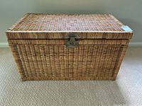 Top front view of a rectangular wicker chest, showing woven wicker lid with a centered metal latch.