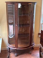 Front view of antique wooden display cabinet with curved glass showing key lock and shelves inside.