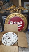 Rheingold wooden beer sign with gold frame and eagle on top, and electric clock inside cardboard box.