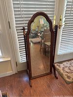 Front view of the vintage wooden swivel floor mirror placed on hardwood floor near white window blinds and door.
