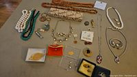 Full collection of assorted jewelry, collectibles, and accessories shown on table including necklaces, pendants, earrings, keychains, medals, whistles and small items.