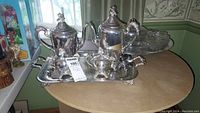 Full view of two silverplated teapots/coffeepots, creamer, sugar bowl, all placed on a rectangular silverplated serving tray with ornate handles.