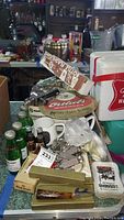 Overview of assorted vintage barware items including boxed mugs, metal openers, and bottles on table surface